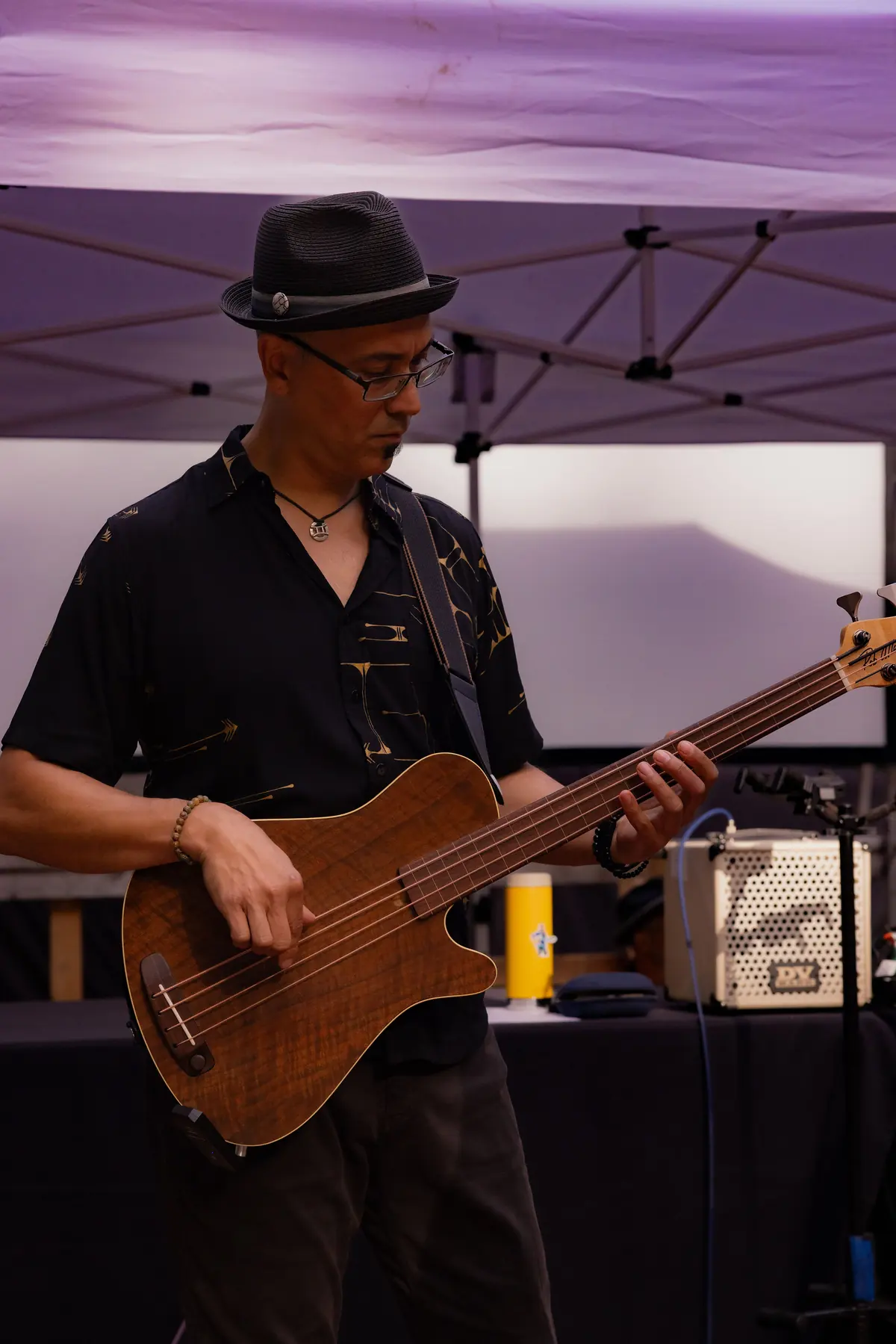 Jason Krivo Flores playing a Rob Allen fretless bass under a canopy, wearing a hat