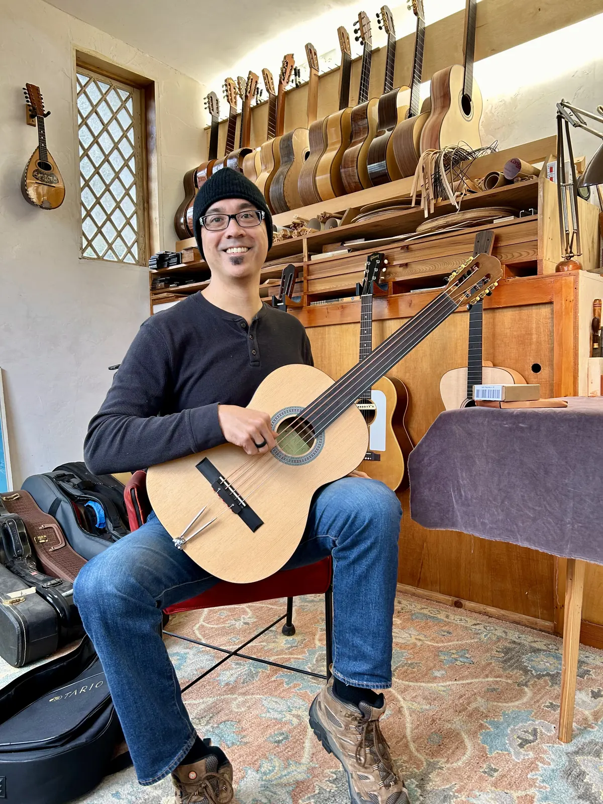 Seated in a luthier&rsquo;s workshop holding the Tario, a fretless classical guitar converted to bass
